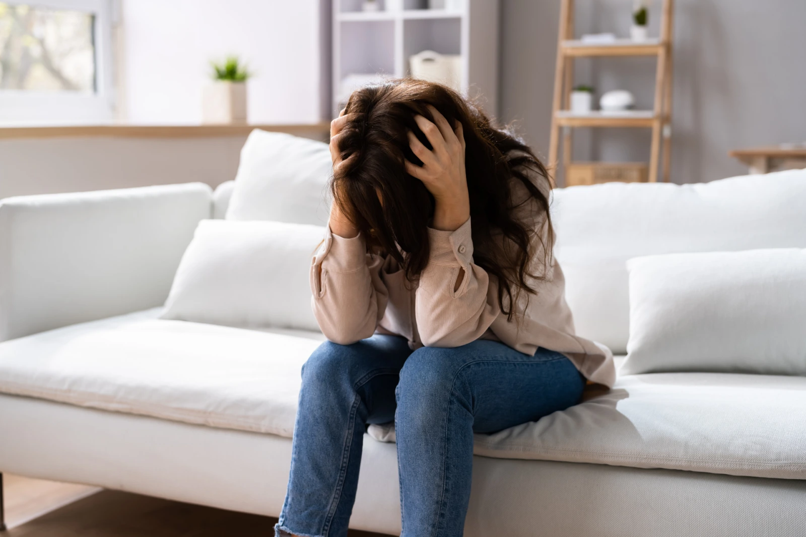 Woman sitting on a couch holding her head, depicting physical stress from anxiety